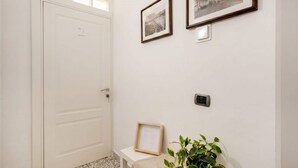 Un pasillo con una puerta blanca, un banco, una planta en maceta y dos cuadros en la pared.