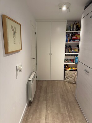 Ein schmaler Flur mit Heizkörper, einem gerahmten Bild an der Wand und einem weißen Kleiderschrank mit geschlossener Tür.