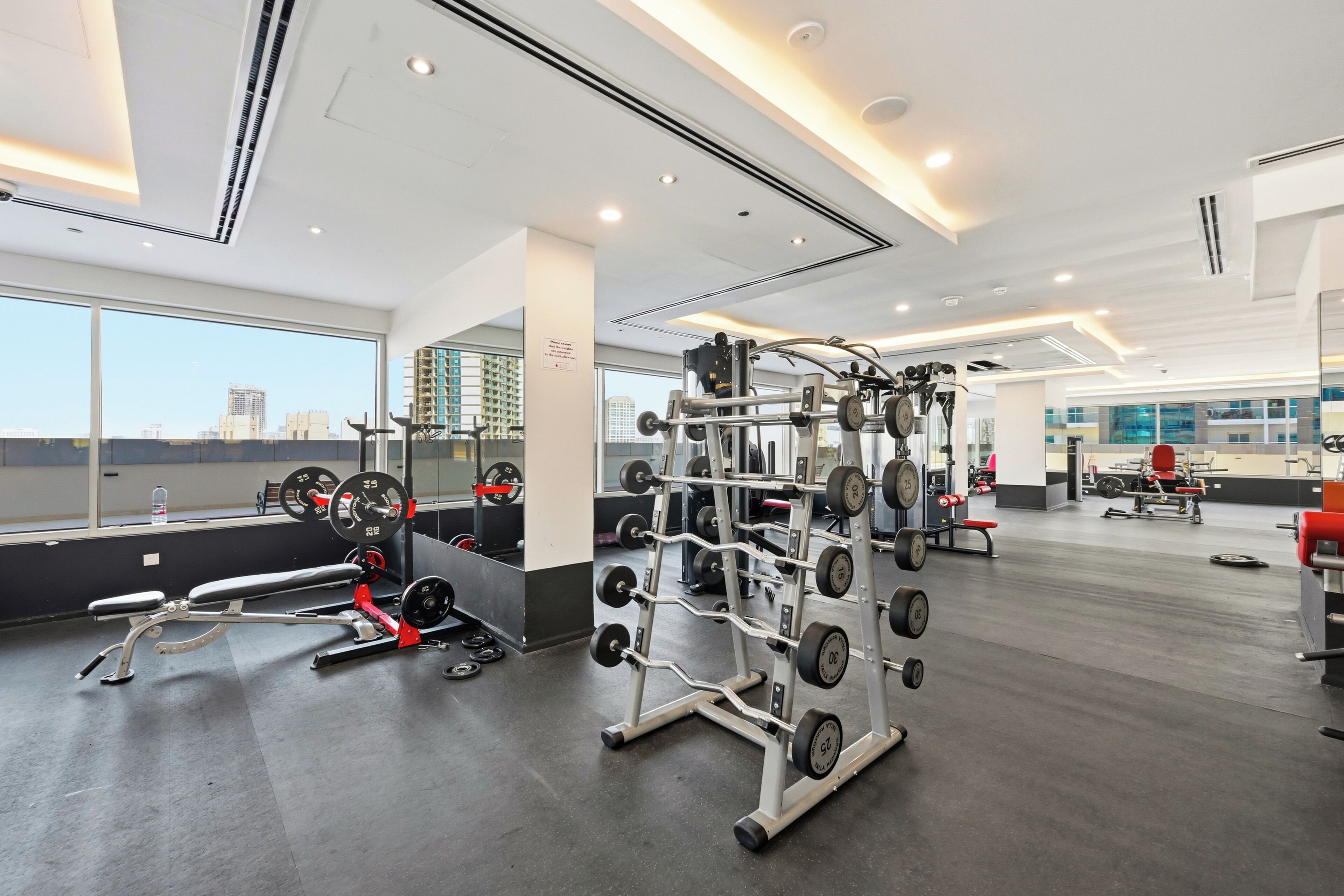 A gym with various exercise equipment, large windows, and a view of the cityscape.