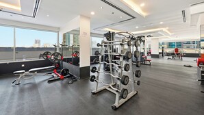 A gym with various exercise equipment, large windows, and a view of the cityscape. - Bloomfields Studio in Hera Tower  (Dubai)