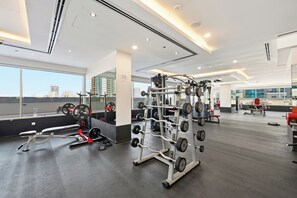 Ein Fitnessstudio mit unterschiedlichen Trainingsgeräten, großen Fenstern und Blick auf die Stadtlandschaft.