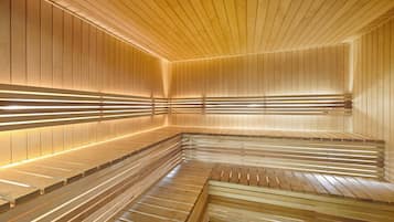 Un sauna avec des bancs en bois et des parois à lattes, éclairé par des luminaires linéaires.