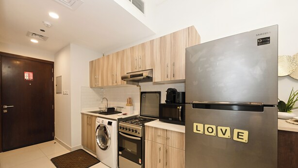 A modern kitchen with wooden cabinets, a stainless steel refrigerator, a washing machine, and a stove. - Bloomfields Studio in Hera Tower  (Dubai)