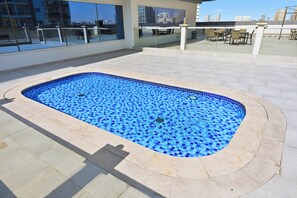 A swimming pool with a blue mosaic tile design, surrounded by a light-colored tiled deck. - Bloomfields Studio in Hera Tower  (Dubai)