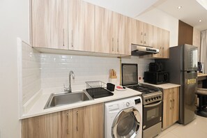 A modern kitchen with wooden cabinets, a stainless steel sink, a microwave, a stove, a refrigerator, and a washing machine. - Bloomfields Studio in Hera Tower  (Dubai)