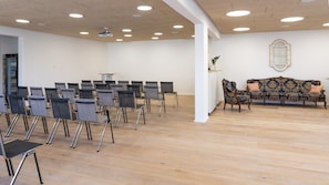 Ein Konferenzraum mit Stuhlreihen, einem Projektor, einer Couch und einem Fenster an der Wand.
