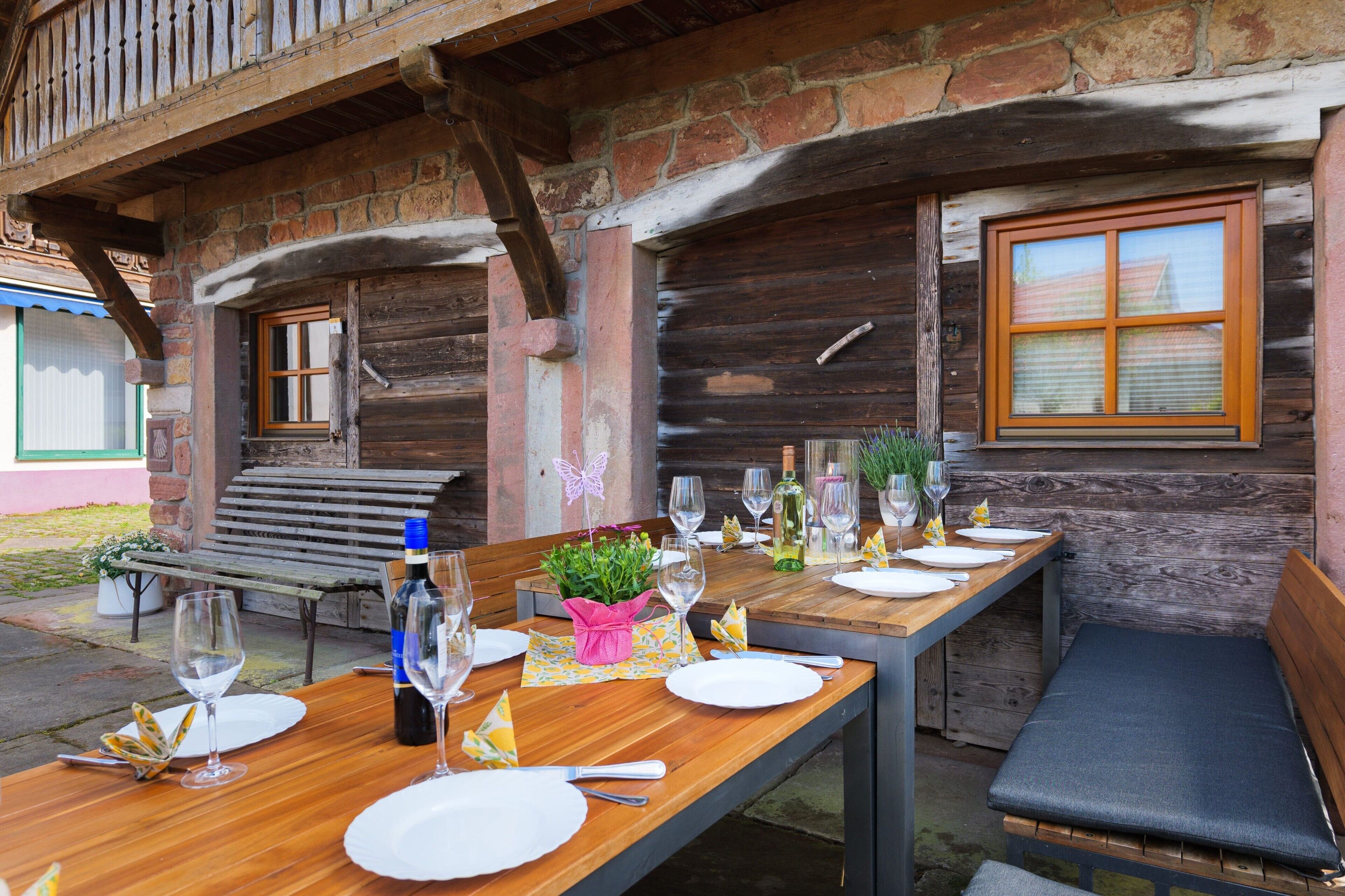 Ein Holztisch draußen gedeckt mit Tellern, Gläsern und Flaschen.