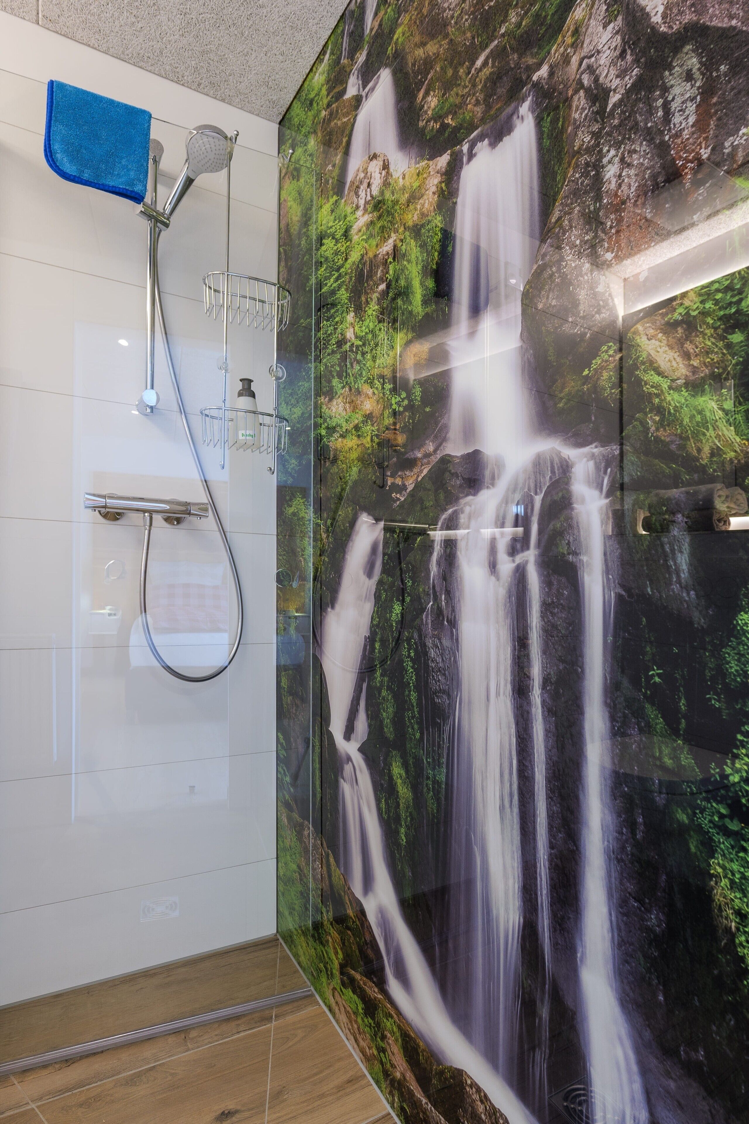 A bathroom with a shower, a towel rack, and a wall mural of a waterfall.