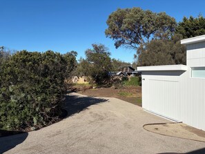A gravel driveway leading to a white building with a garage. - Tiberius House | Brand New Luxury Retreat with Heated Pool, Sauna & Pickleball (Saint Andrews Beach)