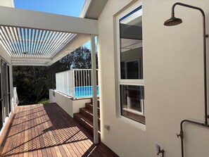 A covered outdoor area with a pool, wooden deck, and a shower. - Tiberius House | Brand New Luxury Retreat with Heated Pool, Sauna & Pickleball (Saint Andrews Beach)