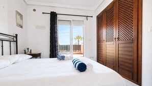 A hotel room with a bed, a window with a view, a wooden door, and a small table. - Altos de la Bahía Spacious Townhouse With Private Garden & Pool (Torrevieja)