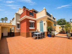 A two-story house with a patio area featuring a table and chairs. - Altos de la Bahía Spacious Townhouse With Private Garden & Pool (Torrevieja)