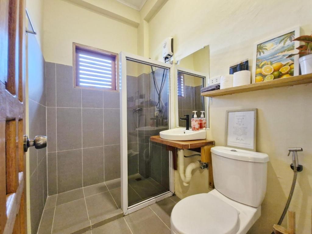 A bathroom with a toilet, a sink, a shower enclosure, and a window with blinds.