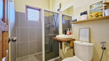 A bathroom with a toilet, a sink, a shower enclosure, and a window with blinds.