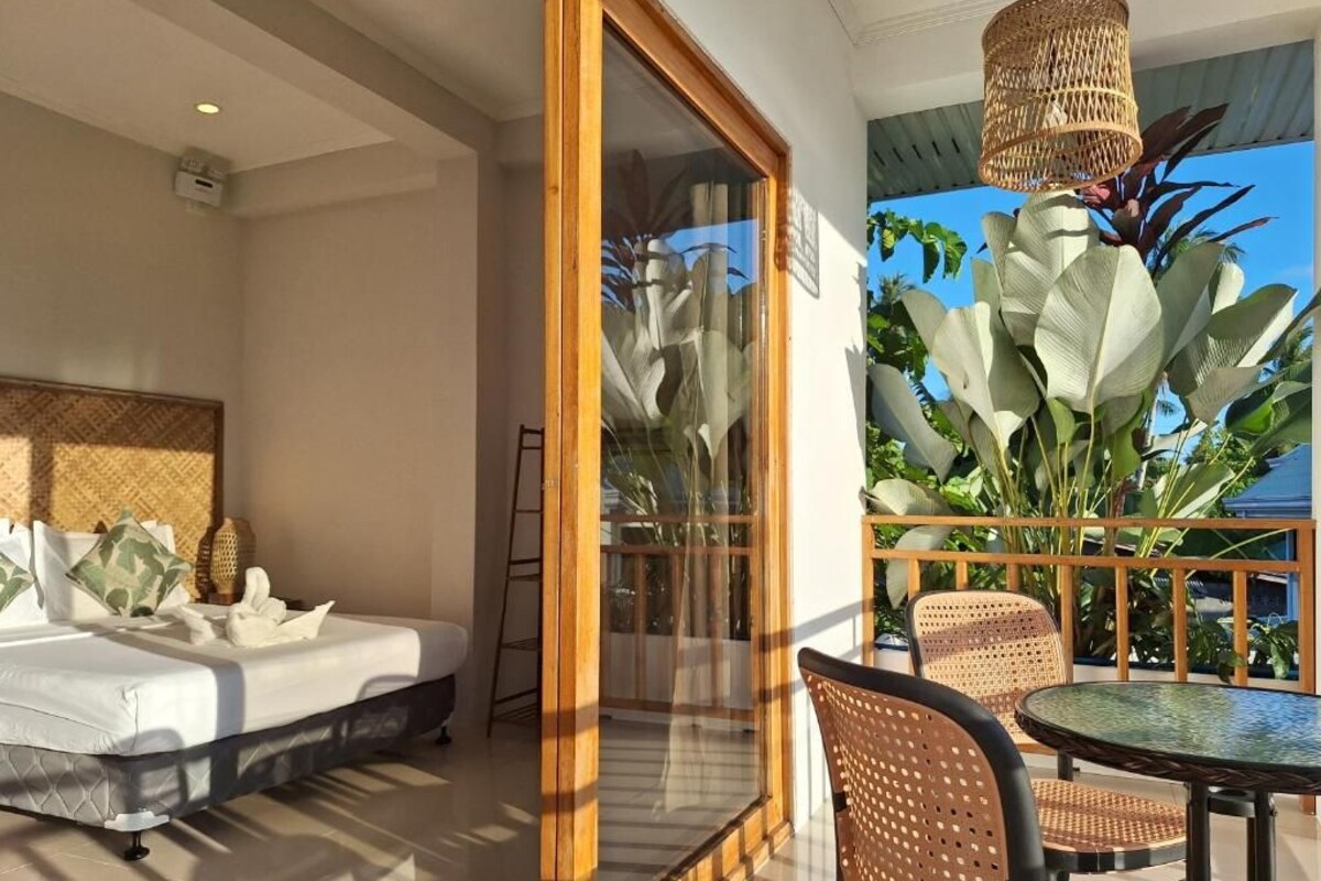 A hotel room with a bed, a balcony with wicker furniture, and a view of the sky.