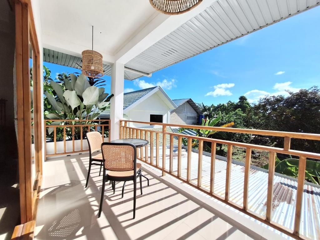 A covered outdoor area with a table and chairs, a railing, and a view of a house and greenery.