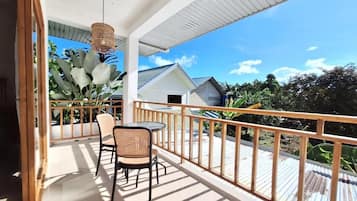 A covered outdoor area with a table and chairs, a railing, and a view of a house and greenery.