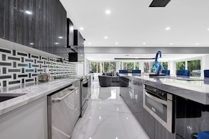 A modern kitchen with a marble countertop, built-in appliances, and a view of the outdoors. - Jungle by the Sea Luxury 5BR Villa (Deerfield Beach)
