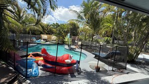 A swimming pool with inflatable slides and lounge chairs, surrounded by palm trees and a fenced area.