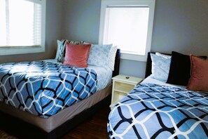 A bedroom with two beds, each with patterned bedding, a nightstand, and a window with blinds. - Jungle by the Sea Luxury 5BR Villa (Deerfield Beach)