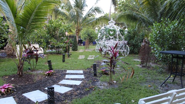 A garden with a white bench, a decorative white structure, and a paved path.