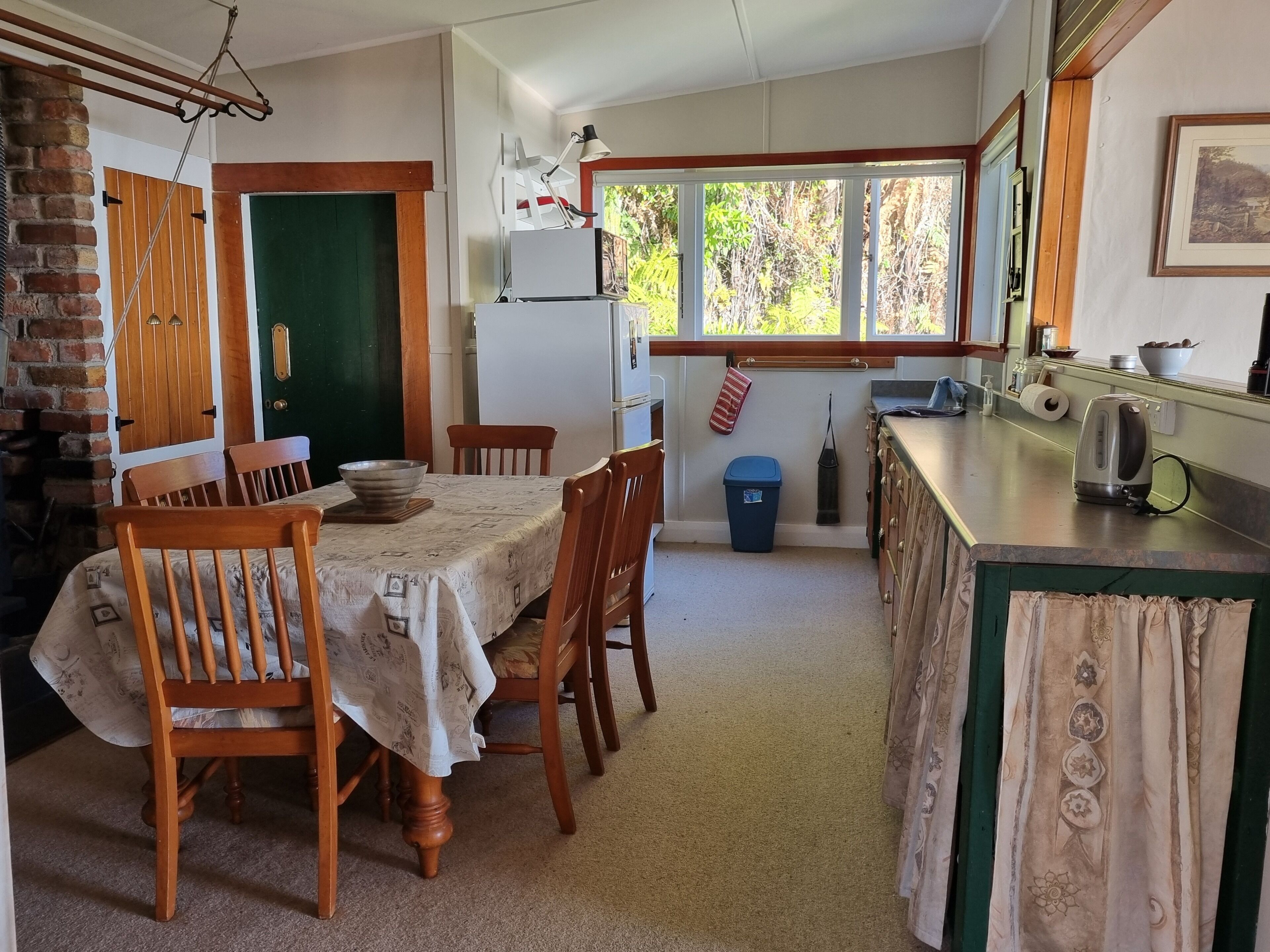 A dining area with a table set for four, a kitchen with a sink and countertop, and a window with a view of greenery.