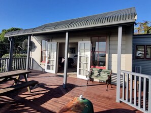 Eine Holzterrasse mit Picknicktisch, einer Bank und einem überdachten Bereich mit offenen Türen.