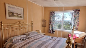 A bedroom with a bed, a dresser, a window with curtains, a wall-mounted lamp, and a framed picture.