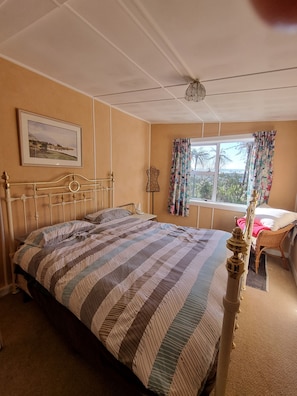 Un dormitori amb un llit, una petarrera, una finestra amb cortines, una làmpada penjada a la paret i un quadre amb marc.
