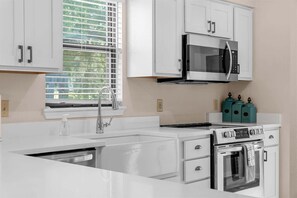 Une cuisine moderne avec des meubles blancs, une cuisinière en acier inoxydable, un four à micro-ondes encastré et une fenêtre équipée de stores.