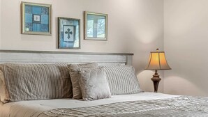 A bed with a striped comforter and pillows, a bedside lamp, and three framed pictures on the wall. - Birdie's Nest and 2bdr Condo (Branson)