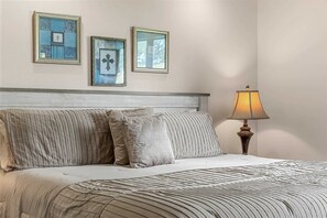 Ein Bett mit gestreiftem Bettbezug und Kissen, eine Nachttischlampe und drei gerahmte Bilder an der Wand.
