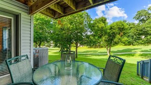 A covered patio with a round glass table and chairs, overlooking a well-manicured lawn and trees. - Birdie's Nest and 2bdr Condo (Branson)