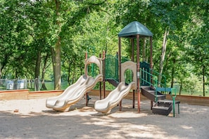 Ein Spielplatz mit zwei Rutschen, einer Kletterkonstruktion und einer kleinen Schutzhütte.