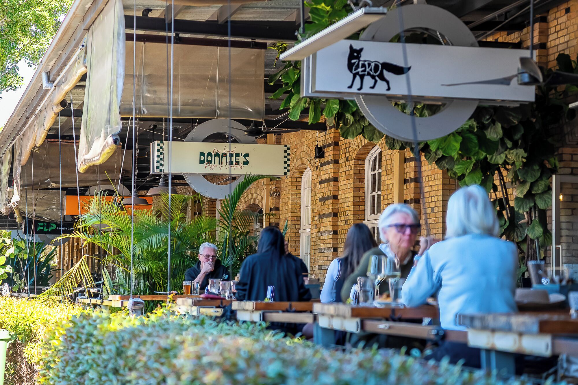 An outdoor seating area with tables and chairs, a hanging sign with a cat logo, and a building with a brick facade in the background.
