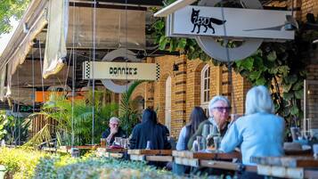 An outdoor seating area with tables and chairs, a hanging sign with a cat logo, and a building with a brick facade in the background.