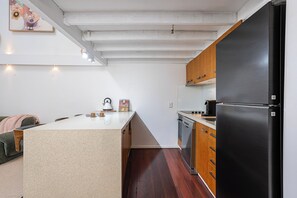 A compact kitchen with a central island, wooden cabinets, and a black refrigerator. - Mactaggarts Place Apartments (Teneriffe)
