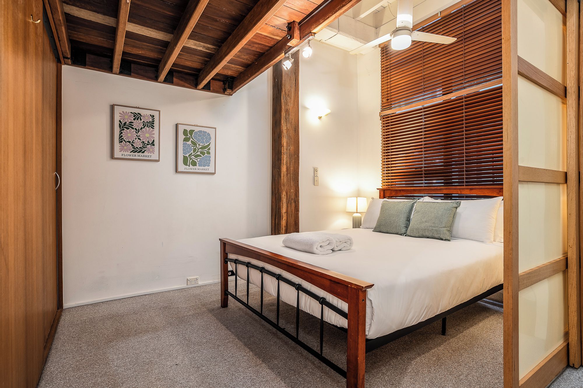 A bedroom with a wooden bed frame, a ceiling fan, and two wall-mounted light fixtures.