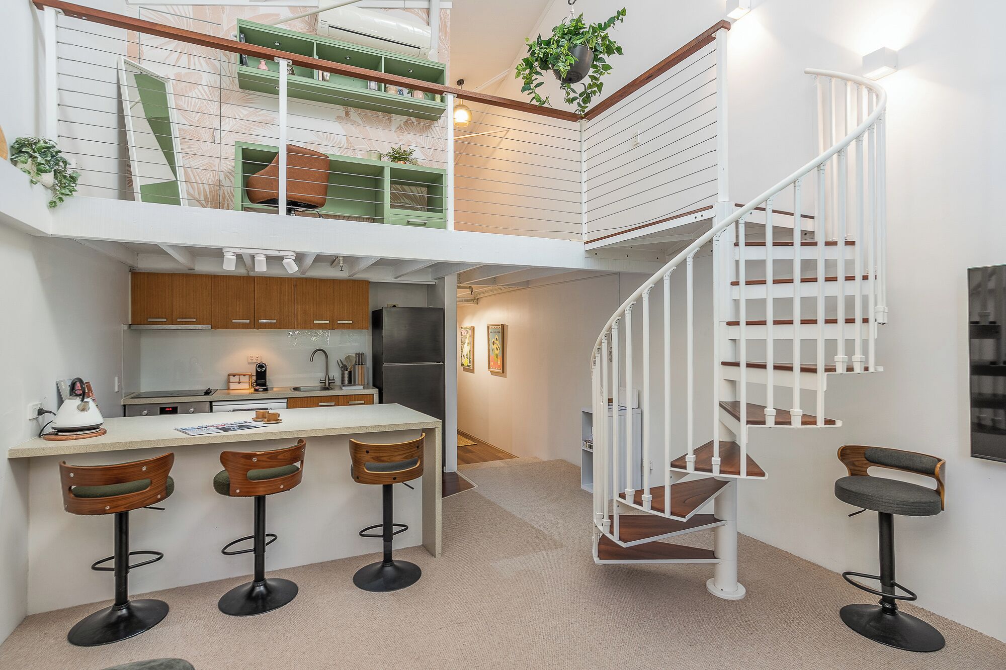 A modern kitchen with a central island, bar stools, a spiral staircase, and a small dining area.