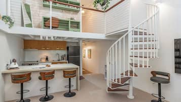 A modern kitchen with a central island, bar stools, a spiral staircase, and a small dining area.