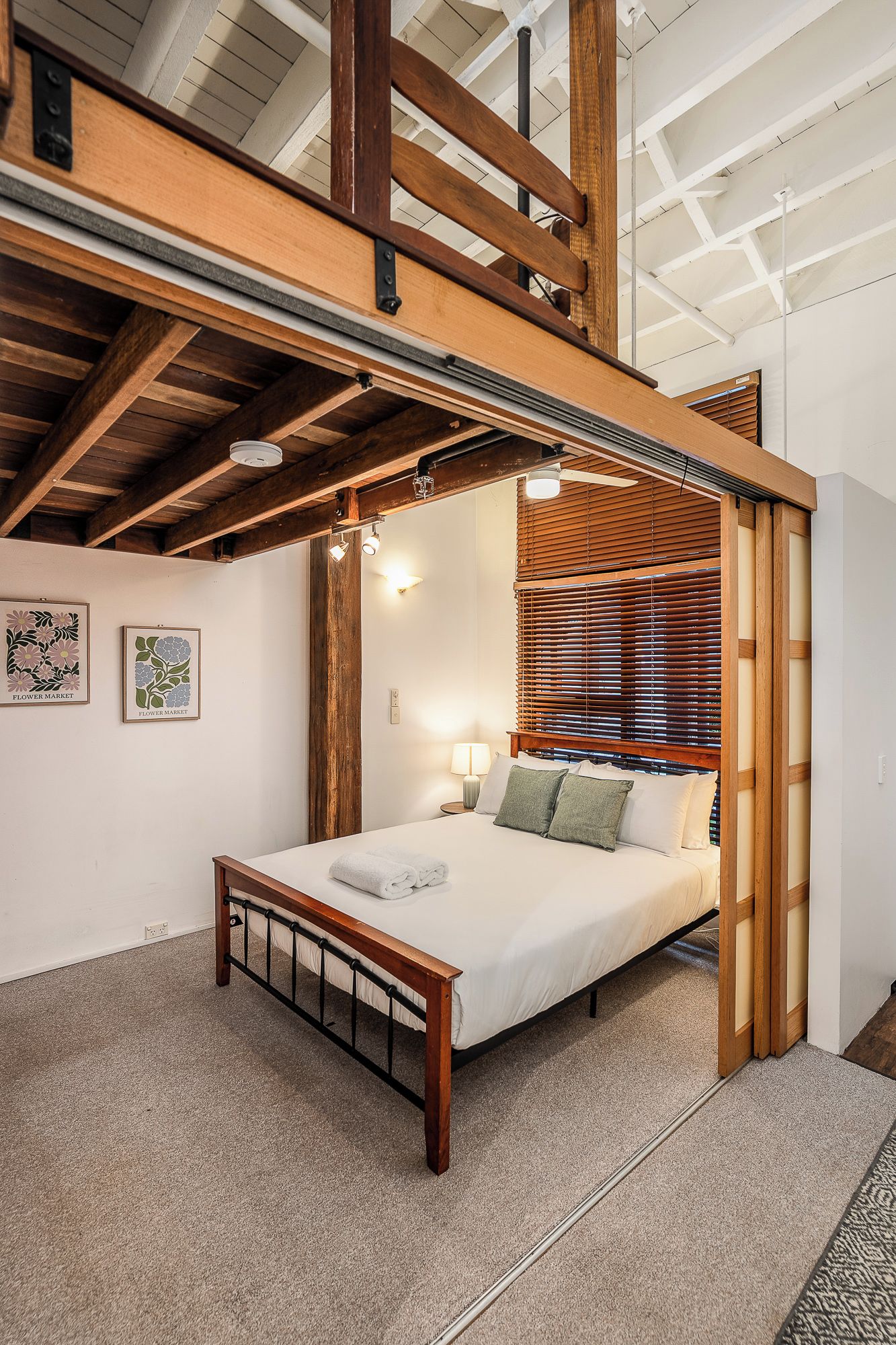 A bedroom with a wooden bed frame, a nightstand, a lamp, and a window with blinds.