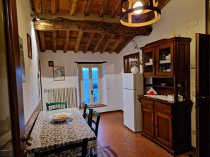 A rustic kitchen with a wooden ceiling, a dining table with chairs, a radiator, and a window with a view. - In Celli, Between the Woods and the Sky - Apartment in an Old Farmhouse Surrounded by Greenery (San Martino in Freddana - Monsagrati)