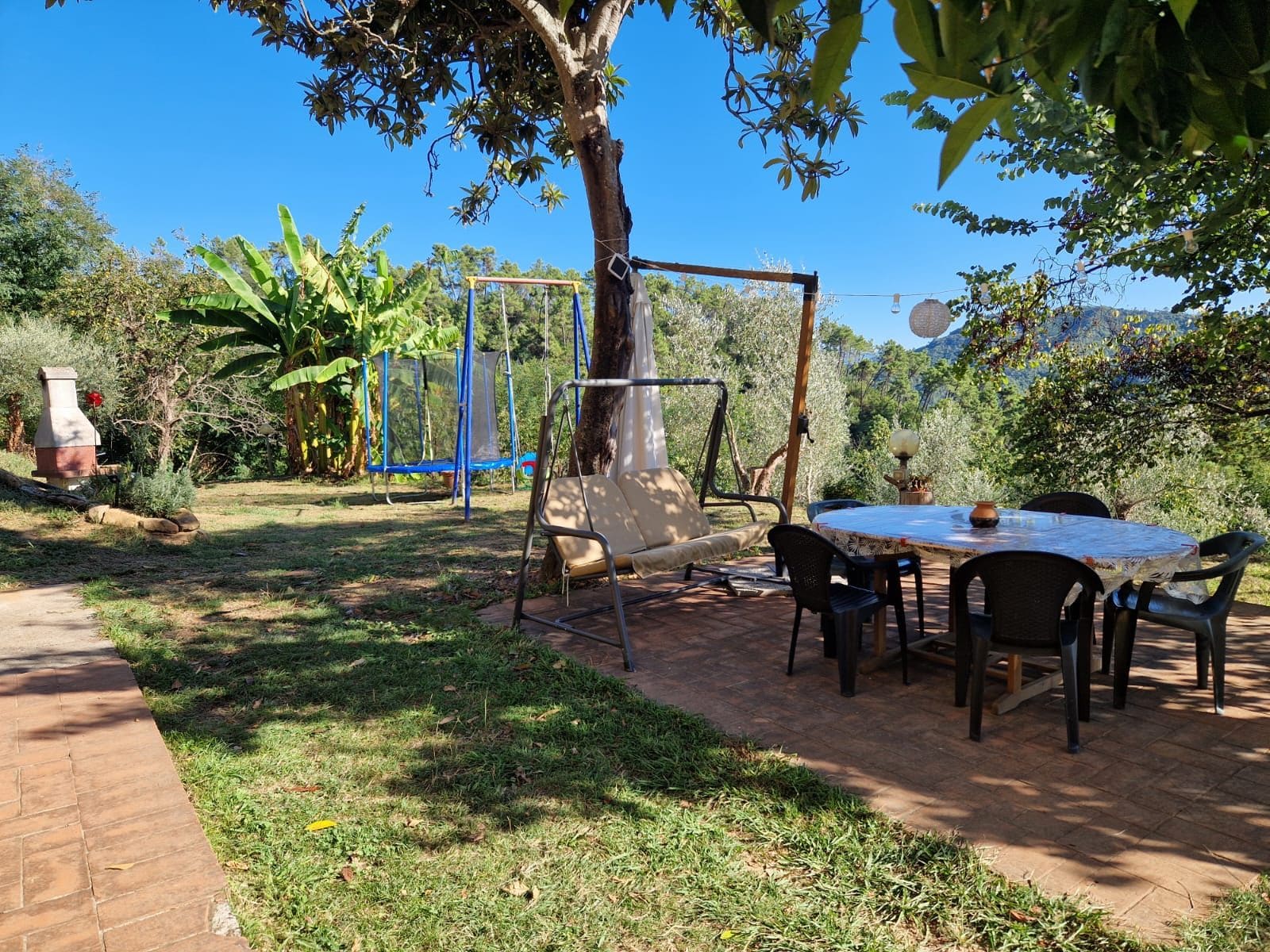 Uma área de pátio com balanço, mesa e cadeiras, e um caminho de tijolos.