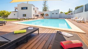 A swimming pool with lounge chairs and a shaded area, surrounded by a modern building.