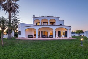 Une maison à deux étages dotée d’un patio couvert, d’un espace salon extérieur et d’une pelouse bien entretenue.