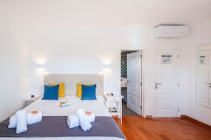 A hotel room with a bed, bedside tables, a nightstand, an air conditioning unit, and a door leading to another room. - Luxury Villa with Heatable Pool and BBQ (Benagil)