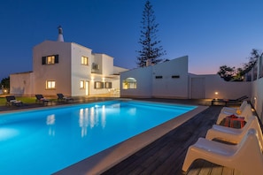 A modern poolside area with a pool, lounge chairs, and a building with multiple windows and a chimney. - Luxury Villa with Heatable Pool and BBQ (Benagil)