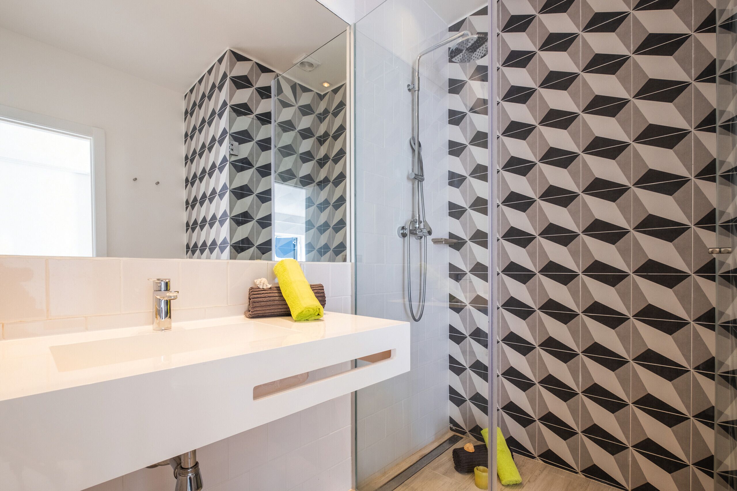 A bathroom with a geometric patterned wall, a white sink with a chrome faucet, and a glass shower enclosure.