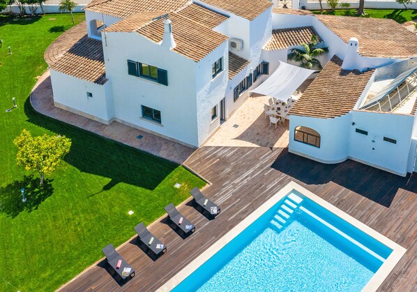 A large house with a swimming pool, a wooden deck, and a well-maintained lawn.