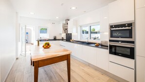 A modern kitchen with white cabinetry, a wooden dining table, and built-in appliances.